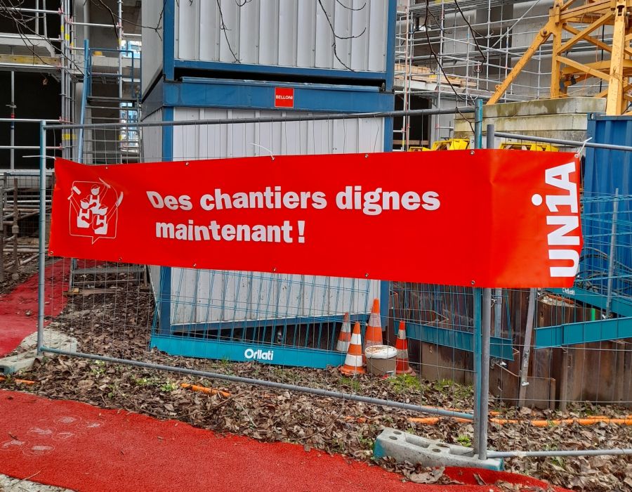 Banderole d'Unia "Des chantiers dignes maintenant!" à l'entrée d'un chantier.