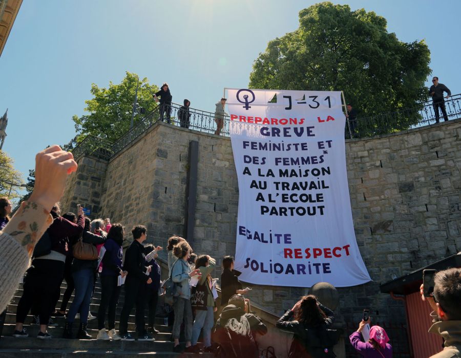 Une septantaine de femmes rassemblées sur la place de la Riponne à Lausanne. A l'arrière une banderole géante sur laquelle on peut lire: "J-31 Préparons la Grève féministe et des femmes à la maison, au travail, à l'école, partout. Egalité, respect, solidarité."