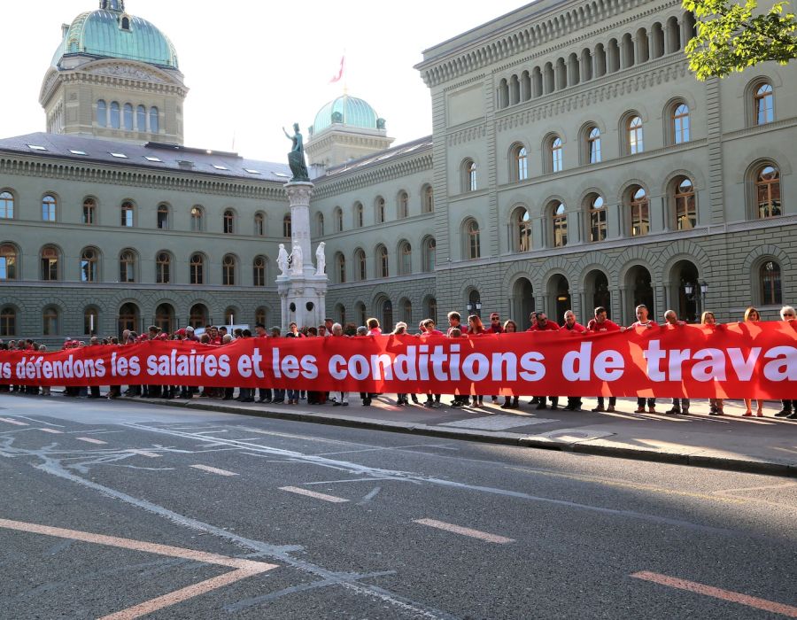 Devant le palais fédéral, une longue banderole rouge Unia sur laquelle on peut lire: "Nous défendons les salaires et les conditions de travail"