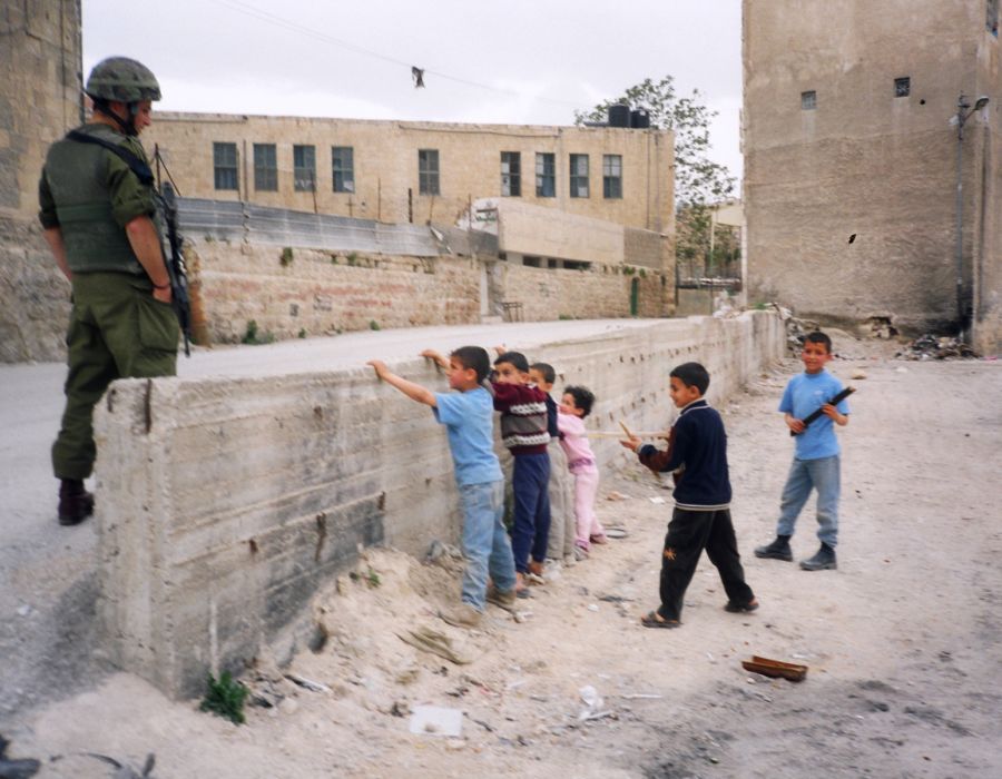 Des enfants jouent à la fouille sous les yeux d'un militaire.