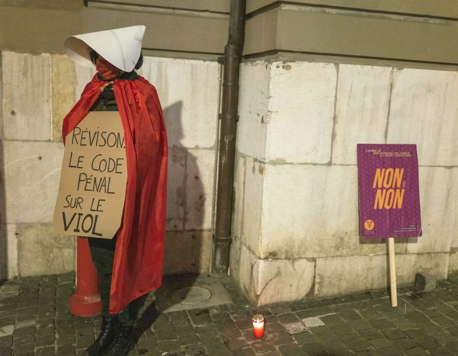 Une femme en costume de "servante écarlate" avec une pancarte "Révisons le code pénal sur le viol".