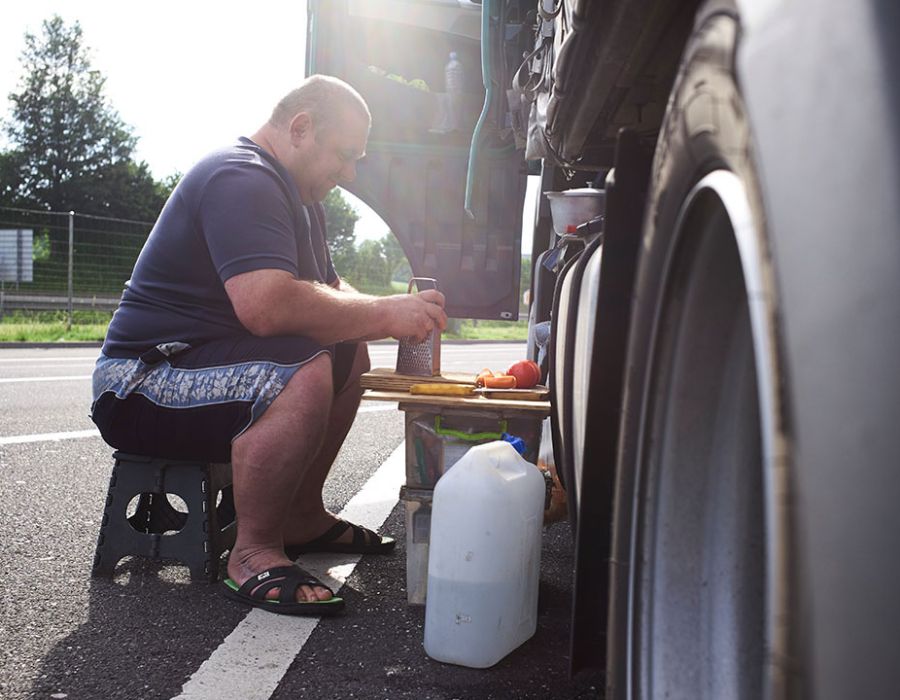 Un routier mange son repas installé sur les flancs de son véhicule.