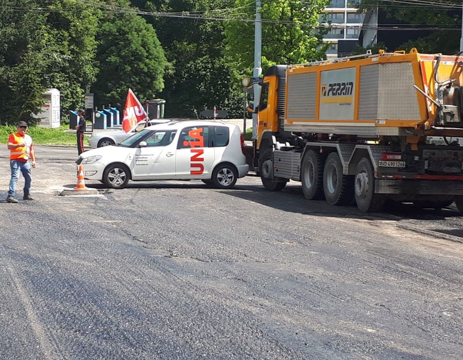 Une voiture d'Unia barre la route à un camion de chantier.