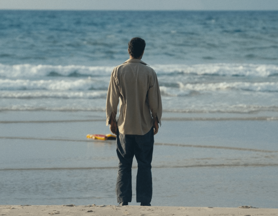 Homme de dos sur une plage, en train de regarder la mer.