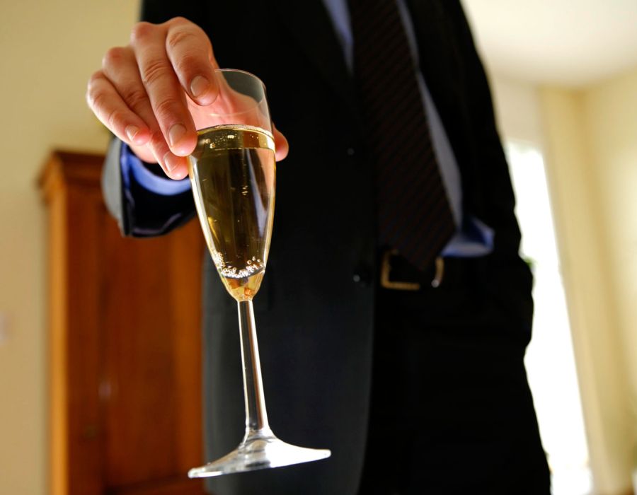 Un homme en costume cravate, une coupe de champagne à la main.