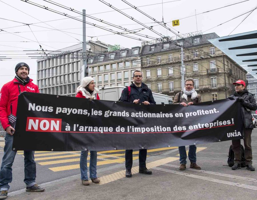 Manifestants tiennent une banderole: "Nous payons, les grands actionnaires en profitent. Non à l'arnaque de l'imposition des entreprises!"