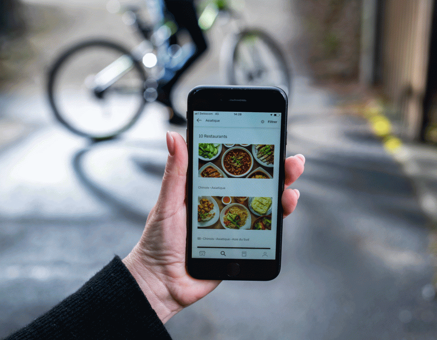 Application Uber Eats ouverte sur un smartphone pointé sur un livreur à vélo.